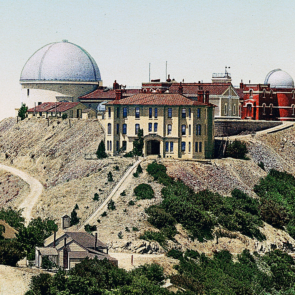 A detail of a print of Lick Observatory, located atop Mt. Hamilton in San Jose, California. The observatory's beautiful buildings are set against a mountain backdrop with lush foliage and a bluish-pink sky.