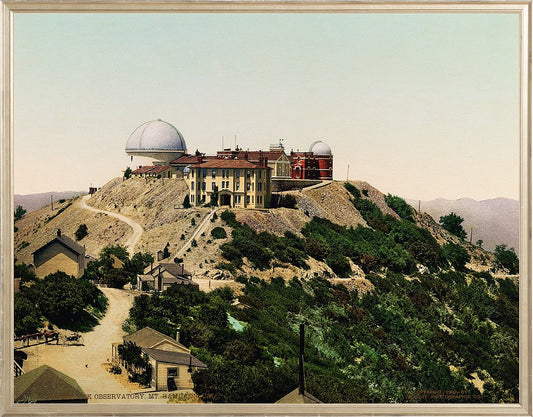 A print of Lick Observatory, located atop Mt. Hamilton in San Jose, California. The observatory's beautiful buildings are set against a mountain backdrop with lush foliage and a bluish-pink sky.